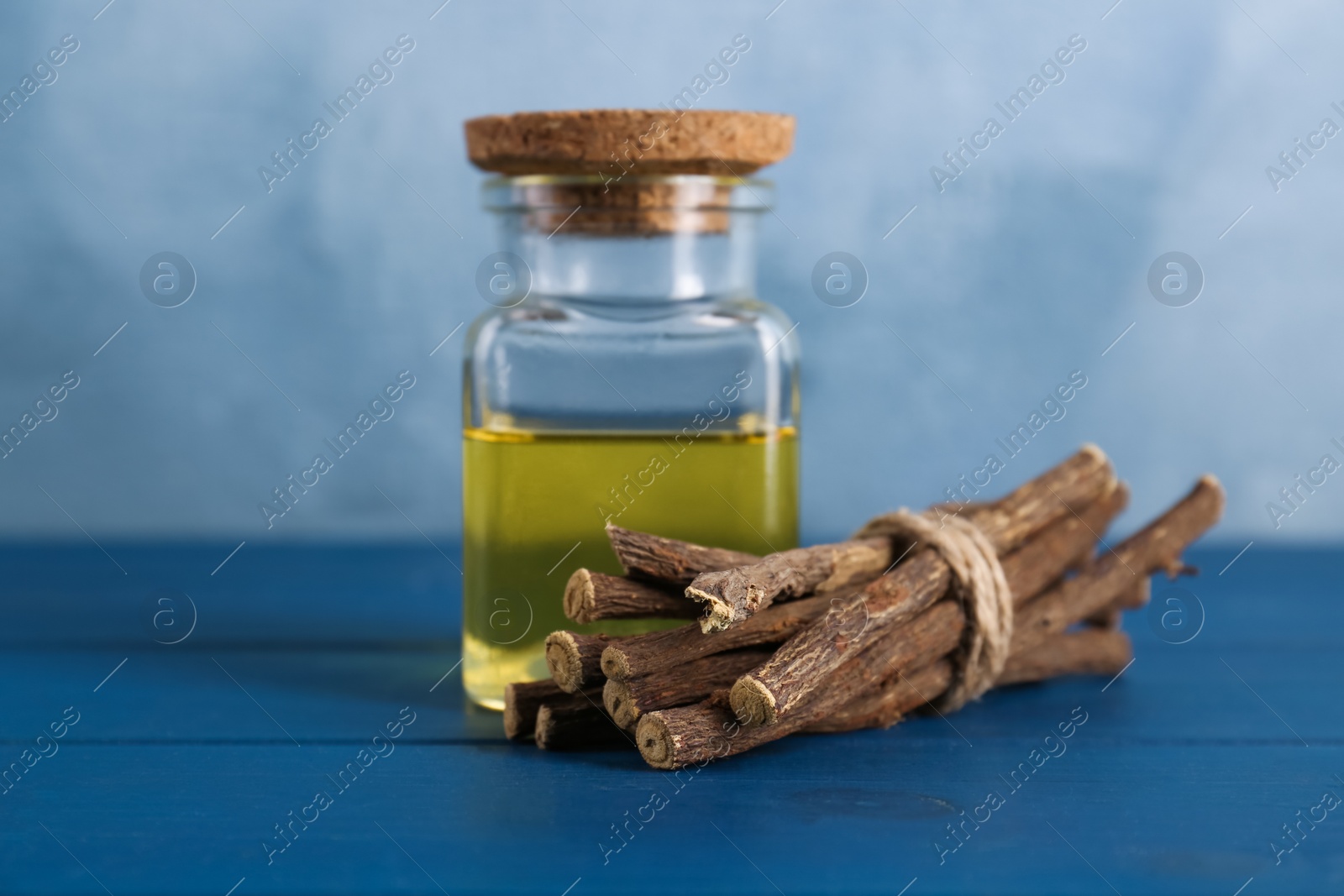 Photo of Dried sticks of licorice root and essential oil on blue wooden table