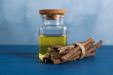 Dried sticks of licorice root and essential oil on blue wooden table