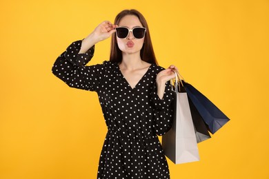 Beautiful young woman with shopping bags on yellow background. Big sale