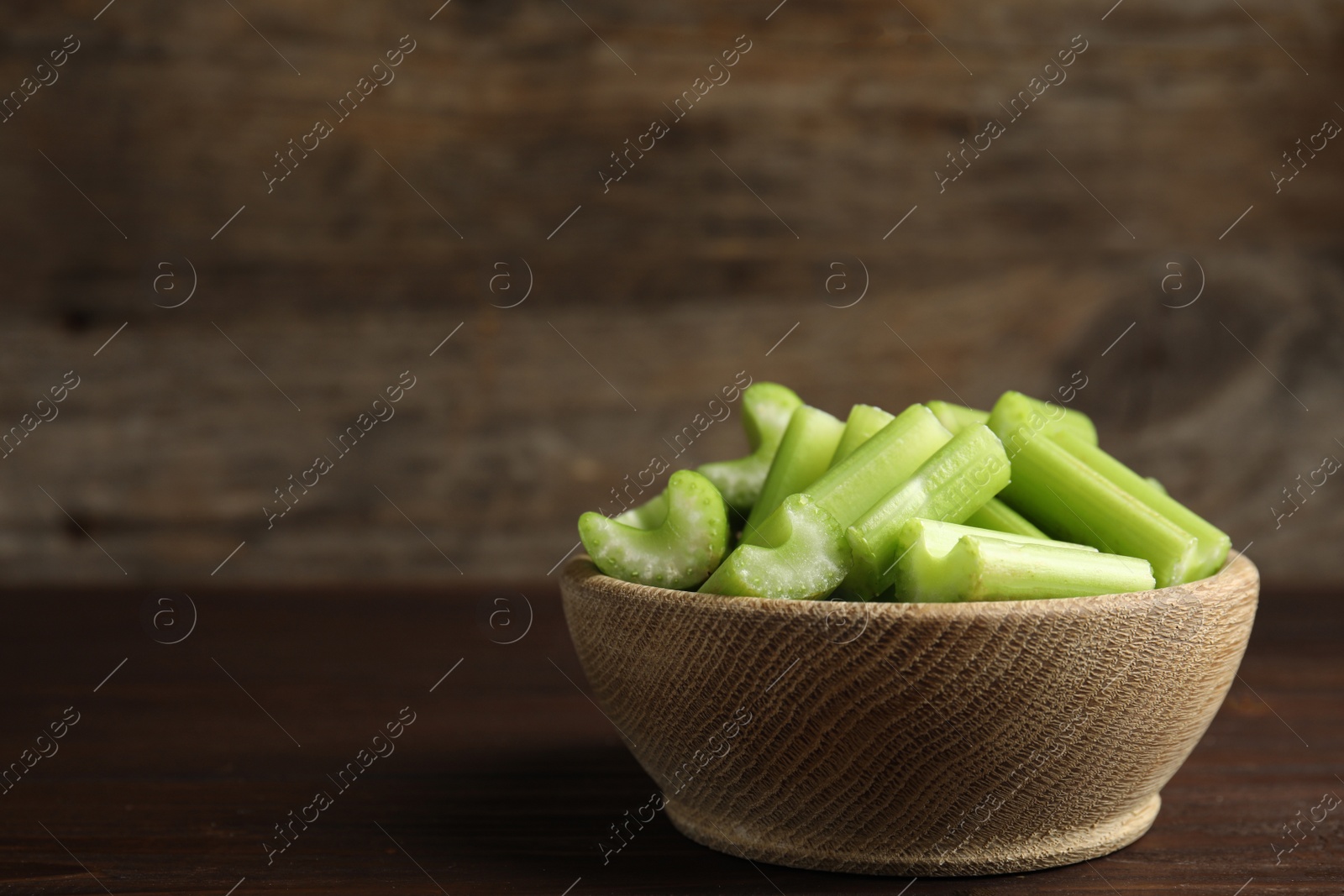 Photo of Cut celery in bowl on wooden table. Space for text