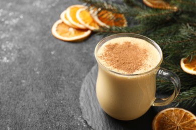 Photo of Glass cup of delicious eggnog with cinnamon on gray table, space for text