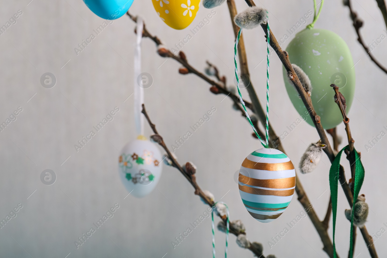 Photo of Closeup view of beautiful willow branches with painted eggs on light blue grey background, space for text. Easter decor