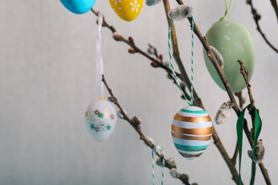 Photo of Closeup view of beautiful willow branches with painted eggs on light blue grey background, space for text. Easter decor