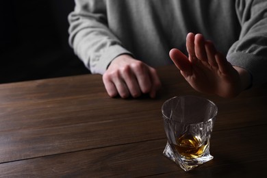 Photo of Man refusing to drink whiskey at wooden table, closeup. Alcohol addiction