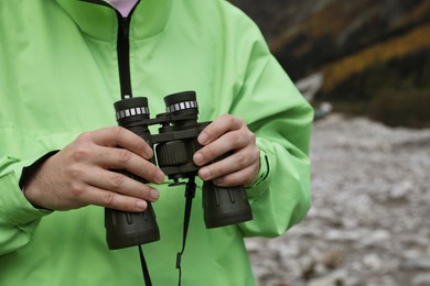 Woman holding binoculars near river in beautiful mountains, closeup. Space for text