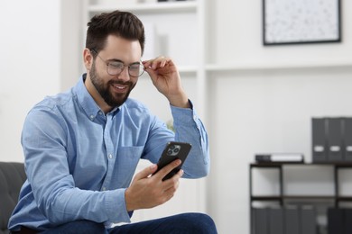 Photo of Handsome young man using smartphone in office, space for text