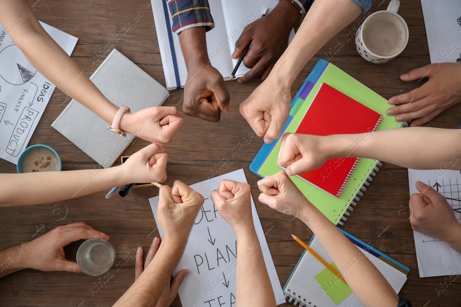 Photo of People putting fists together at table, top view. Unity concept