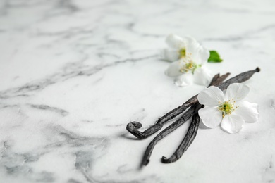 Aromatic vanilla sticks and flowers on marble background, space for text