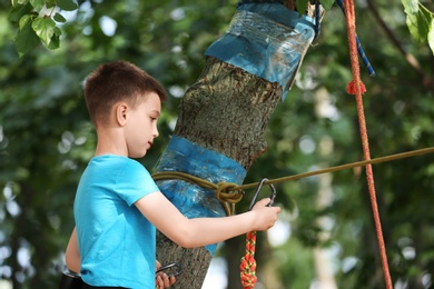 Little boy climbing in adventure park, space for text. Summer camp