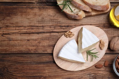 Tasty cut brie cheese with rosemary, bread and nuts on wooden table, flat lay. Space for text