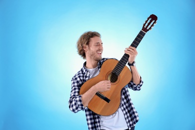 Young man playing acoustic guitar on color background