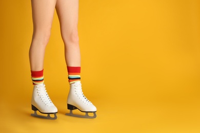 Photo of Woman in elegant white ice skates on yellow background, closeup of legs. Space for text