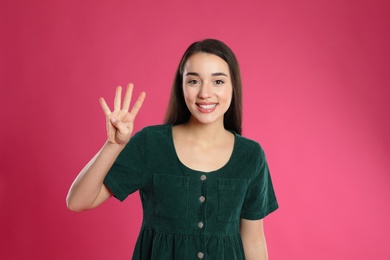 Woman showing number four with her hand on pink background