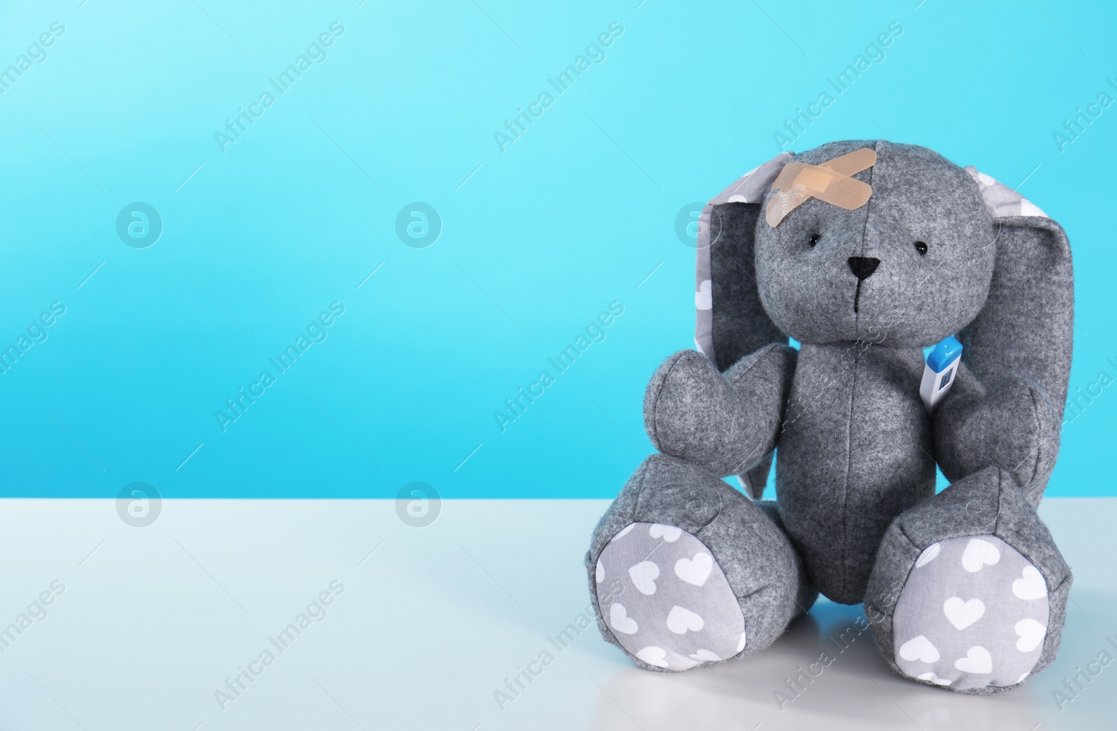 Photo of Toy bunny with thermometer on table against color background, space for text. Children's hospital