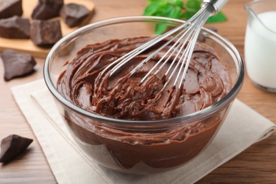 Photo of Whipping chocolate cream with balloon whisk on wooden table, closeup