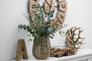 Photo of Beautiful eucalyptus branches on mantelpiece in modern room. Interior design