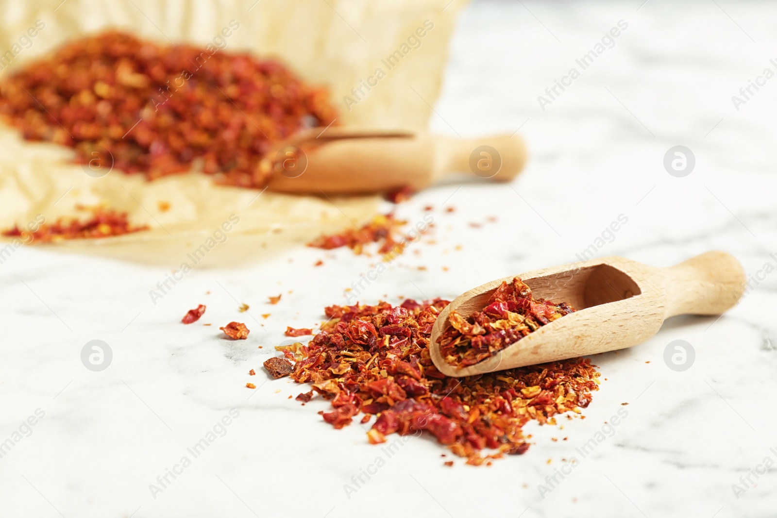 Photo of Wooden scoop and chili pepper flakes on table