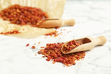 Photo of Wooden scoop and chili pepper flakes on table