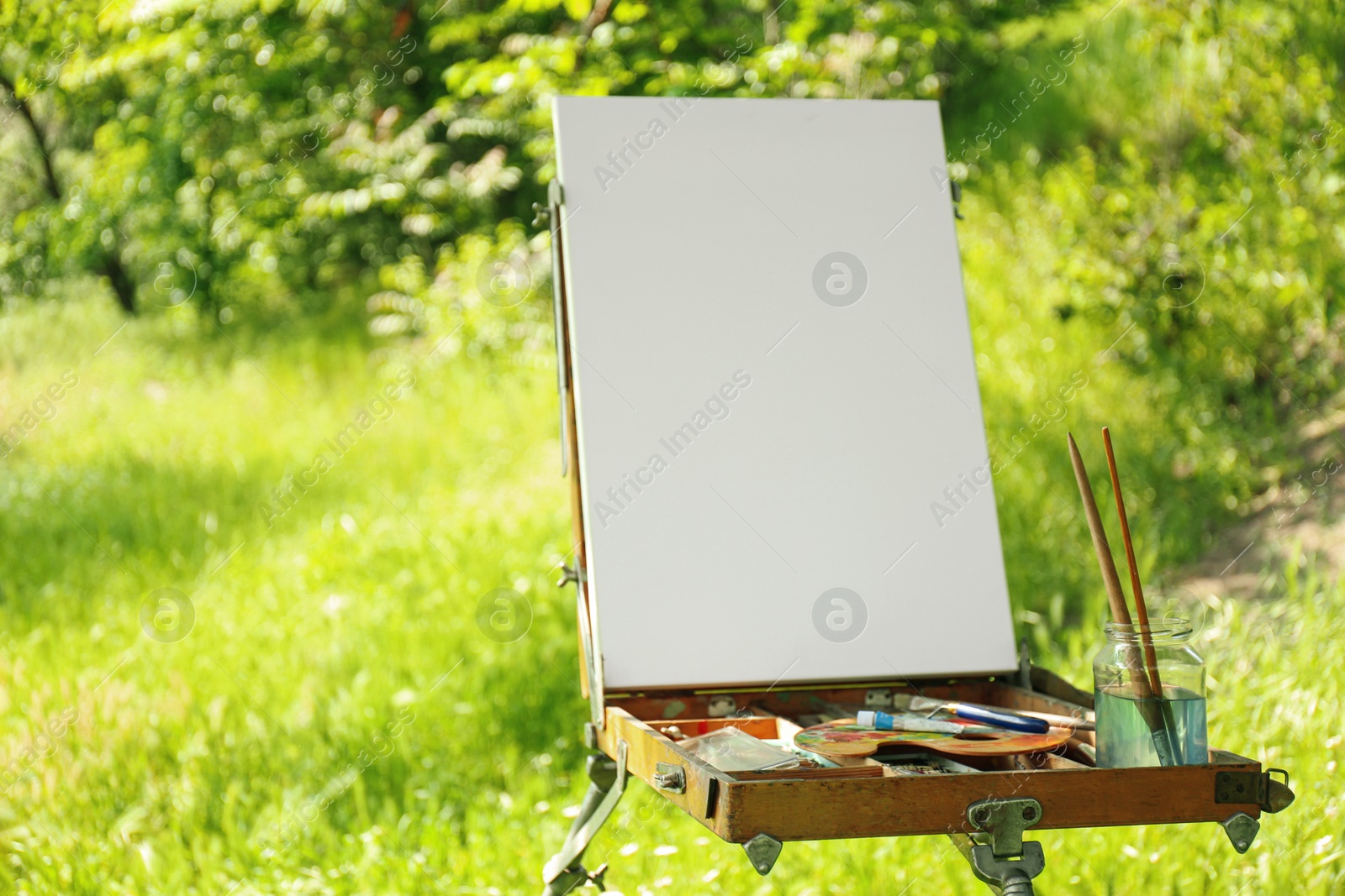 Photo of Easel with blank canvas and painting equipment in countryside