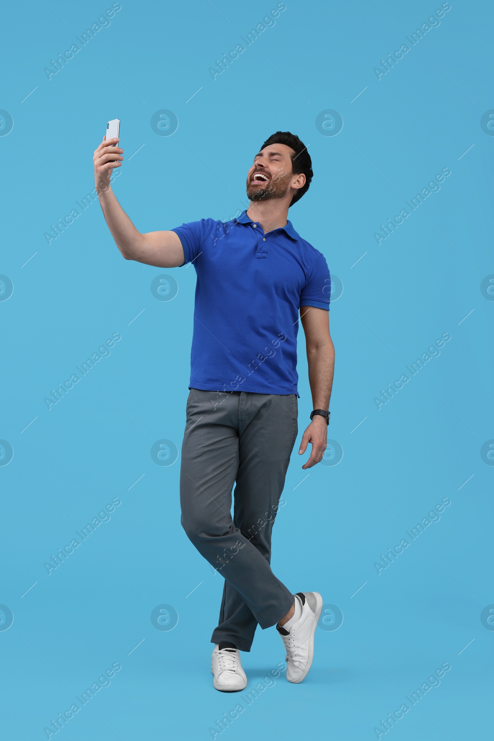 Photo of Smiling man taking selfie with smartphone on light blue background