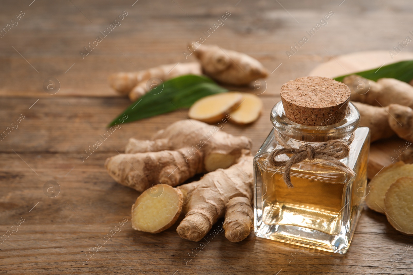 Photo of Glass bottle of essential oil and ginger root on wooden table, space for text