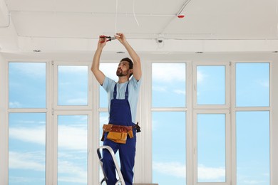 Photo of Electrician with pliers repairing ceiling wiring indoors