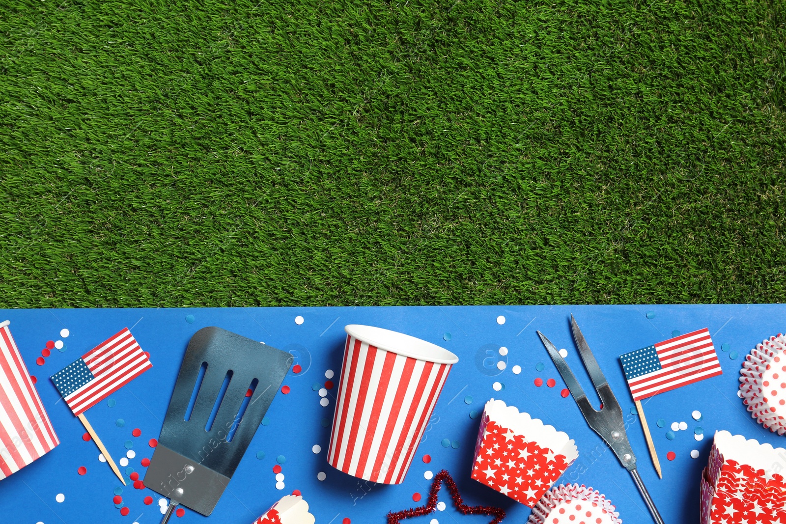 Photo of Flat lay composition with barbecue tools on green grass, space for text. USA Independence Day