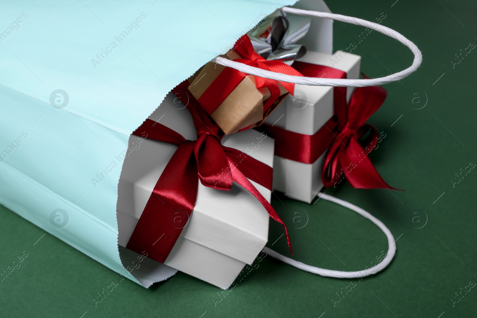 Photo of Turquoise paper shopping bag full of gift boxes on green background, closeup