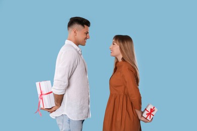 Photo of Lovely couple exchanging gifts on light blue background. Valentine's day celebration