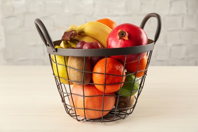 Photo of Fresh ripe fruits in metal basket on wooden table