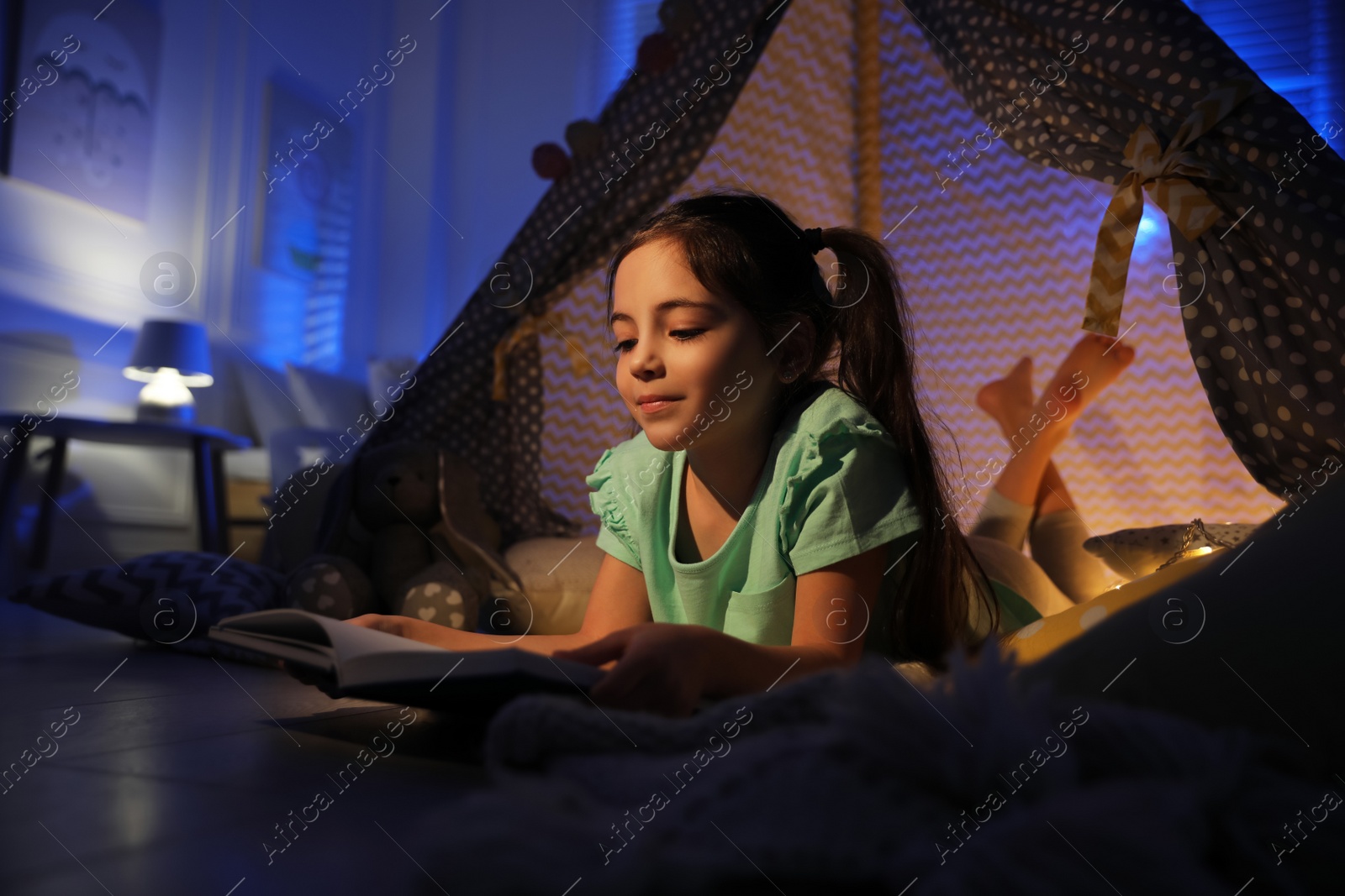 Photo of Little girl reading fairy tale in play tent at home