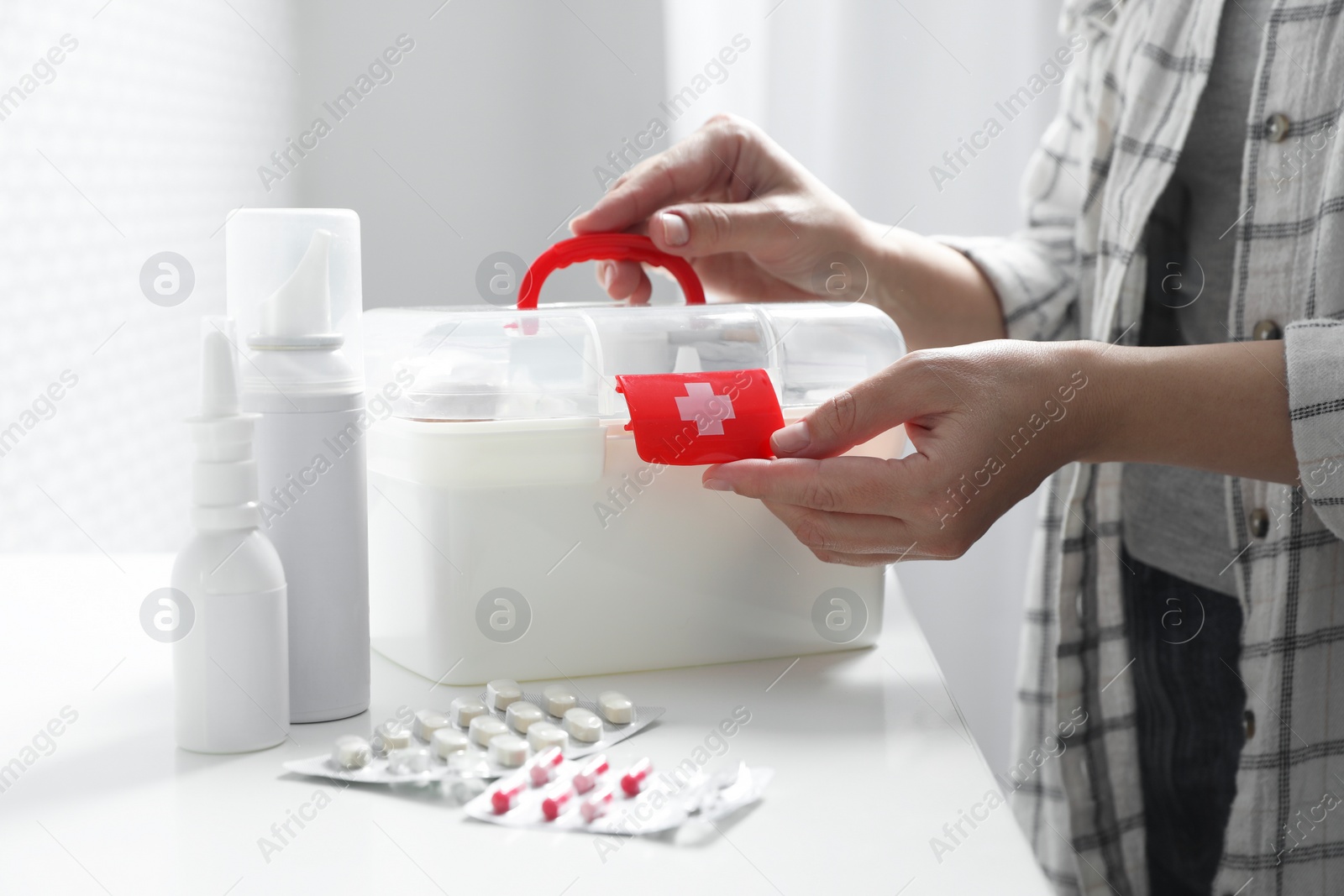 Photo of Woman opening first aid kit at white table indoors, closeup