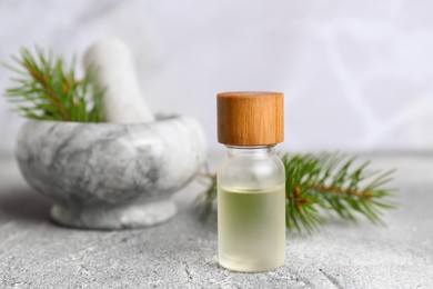 Photo of Bottle of aromatic essential oil and mortar with pine branch on light grey table, closeup