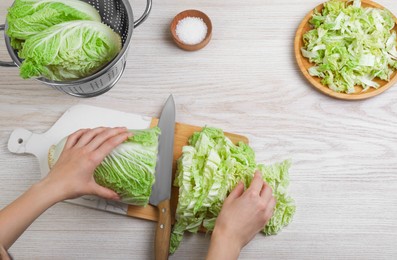 Photo of Woman cutting Chinese cabbage at white wooden kitchen table, top view
