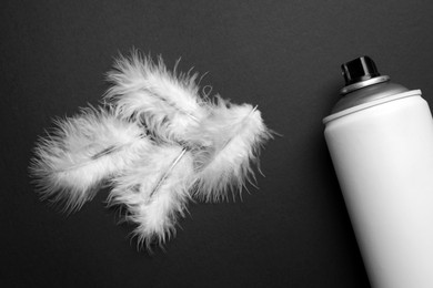 Can of spray paint and feathers on black background, flat lay. Graffiti supply