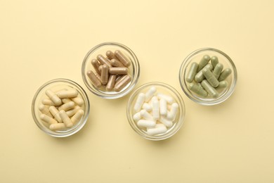 Photo of Different vitamin capsules in bowls on pale yellow background, flat lay