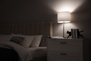 Stylish lamp, books and magazine on bedside table indoors. Bedroom interior elements