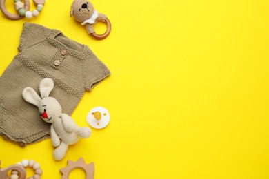 Baby clothes and accessories on yellow background, flat lay. Space for text