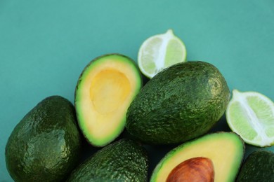 Tasty whole and cut avocados with lime on turquoise background, closeup