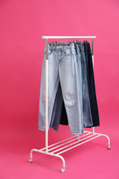 Rack with stylish jeans on pink background