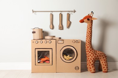 Photo of Cardboard kitchen, washing machine and toy giraffe near white wall indoors