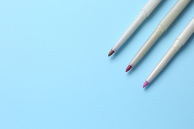 Different lip pencils on light blue background, flat lay with space for text. Cosmetic product