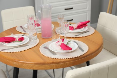 Photo of Color accent table setting. Glasses, plates, jug of beverage and pink napkins in dining room