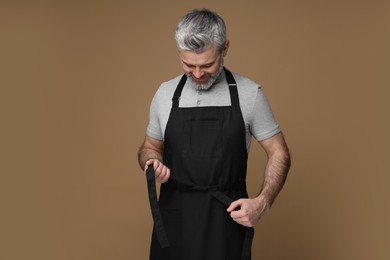 Man wearing kitchen apron on brown background. Mockup for design