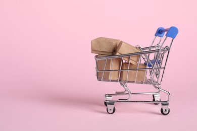 Photo of Small metal shopping cart with cardboard boxes on pink background, space for text
