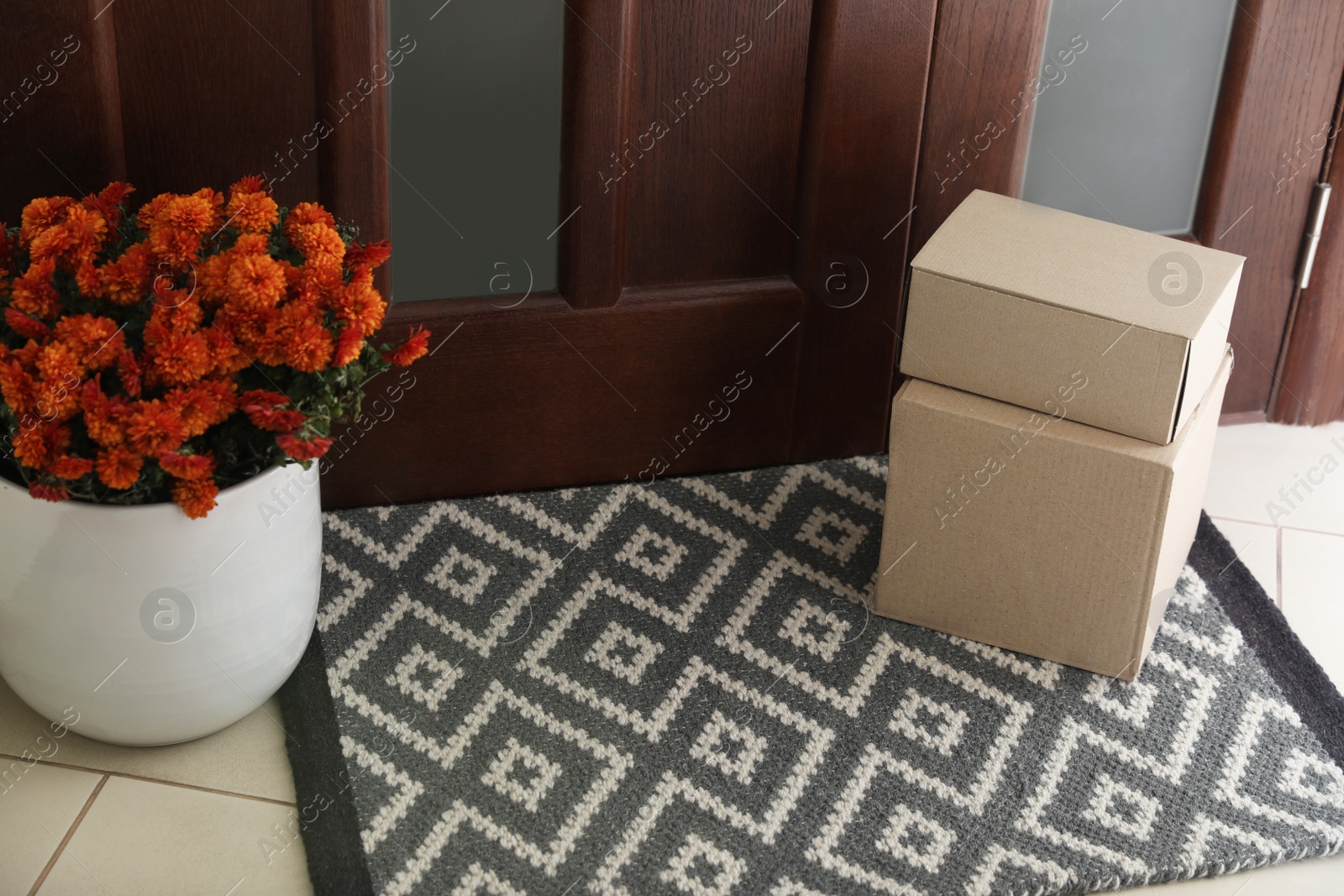 Photo of Cardboard boxes on stylish door mat and beautiful flowers near entrance