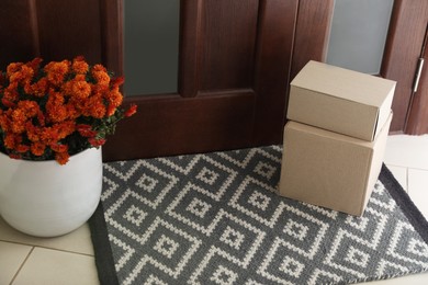 Photo of Cardboard boxes on stylish door mat and beautiful flowers near entrance