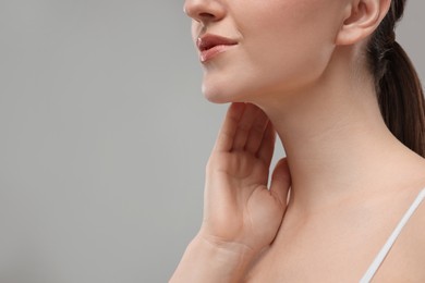 Woman touching her neck on grey background, closeup. Space for text