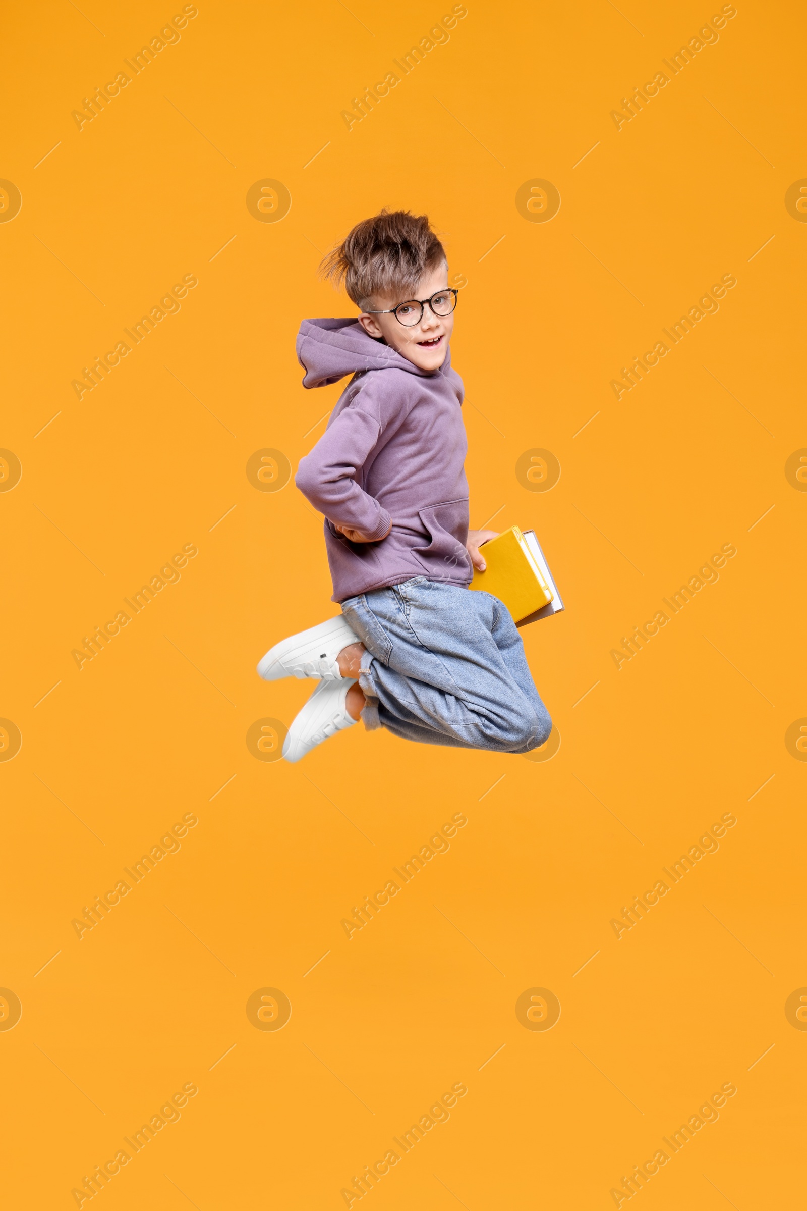 Photo of Cute schoolboy with books jumping on orange background, space for text