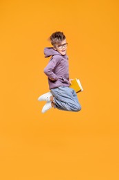 Photo of Cute schoolboy with books jumping on orange background, space for text